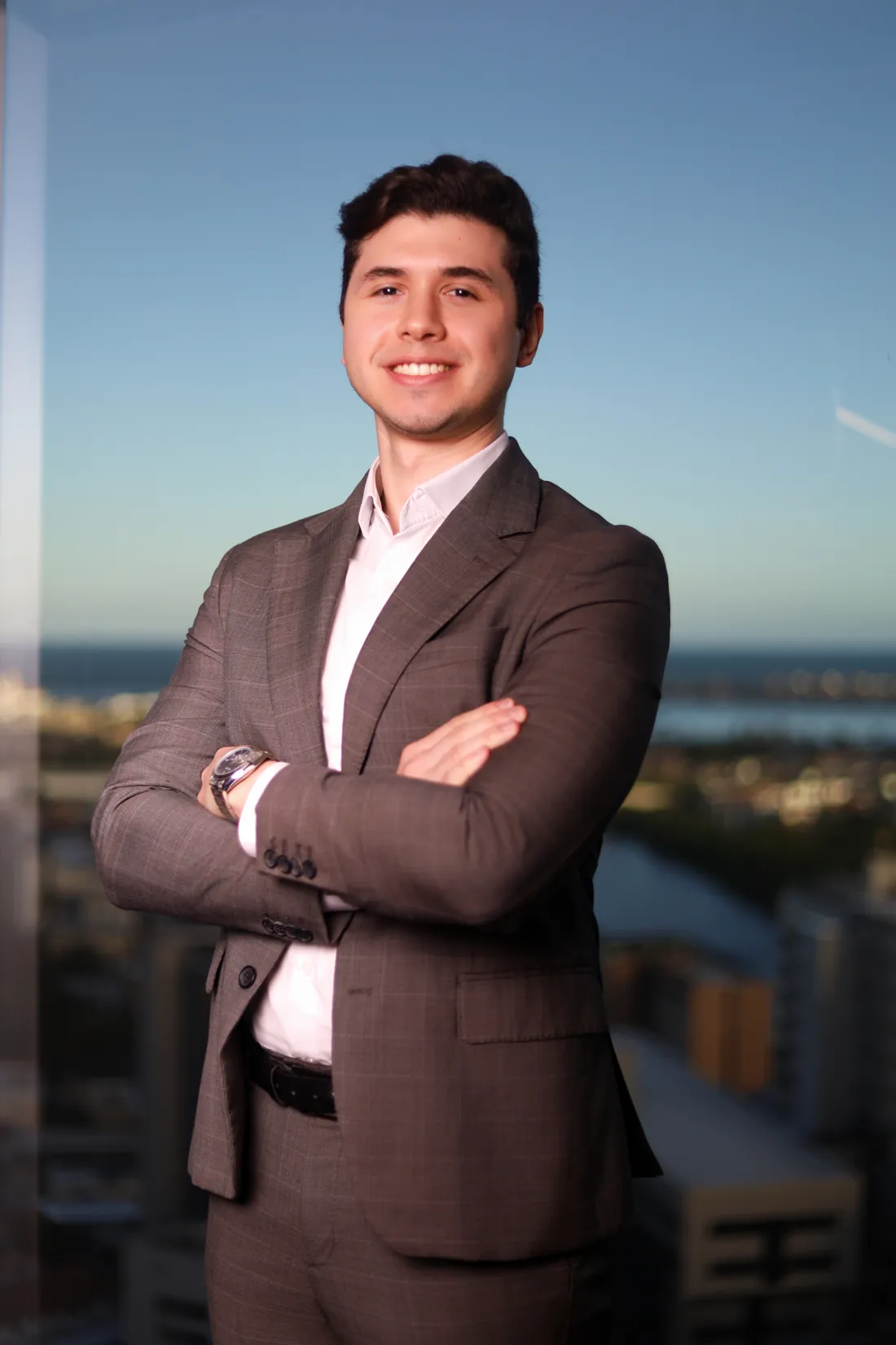 Leonardo França sorrindo, de braços cruzados, em escritório com vista para a cidade